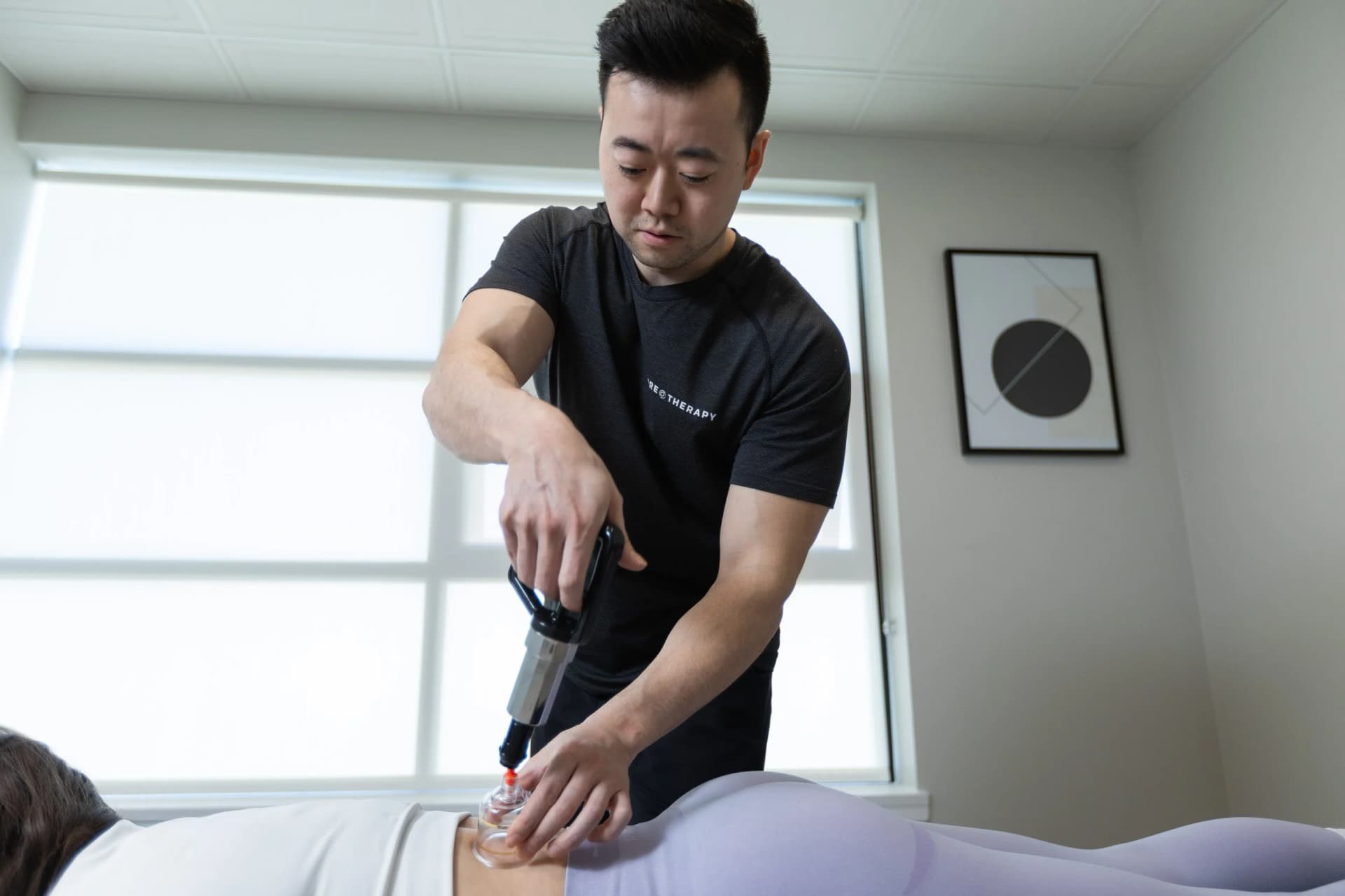A therapist uses a suction pump to apply a cupping cup to a patient's lower back on a treatment table.