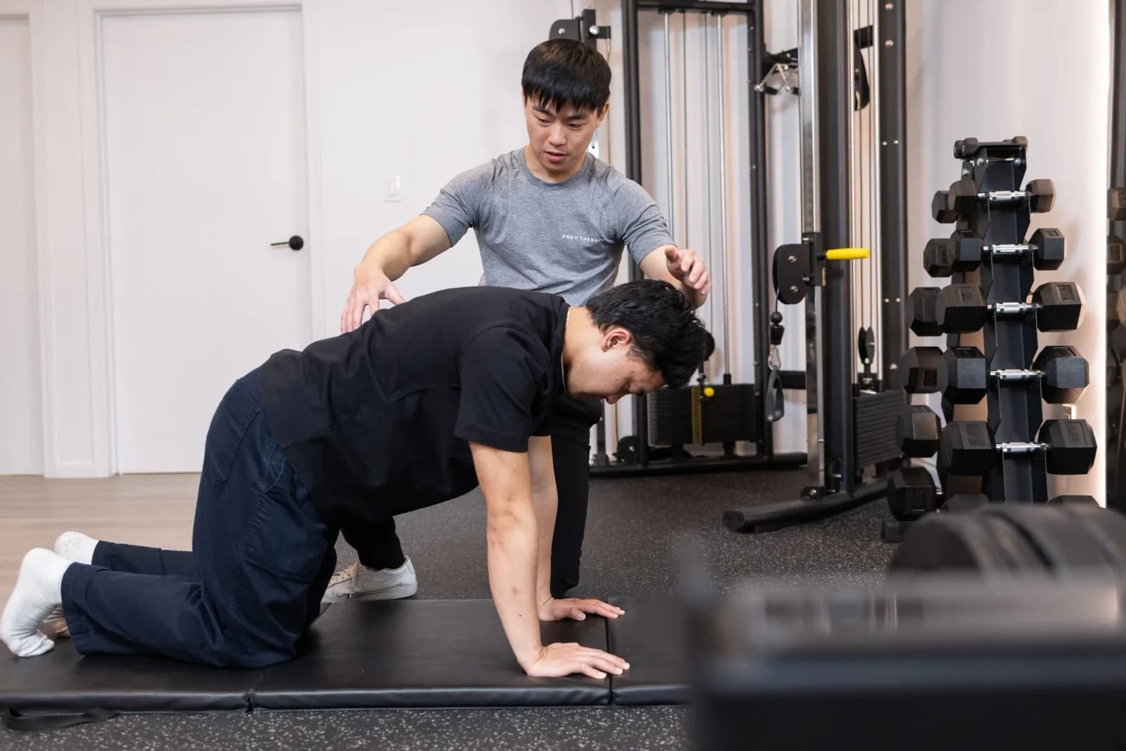 Kinesiologist guiding an athlete through a bird-dog core stability exercise in the PRE Therapy active rehab gym.