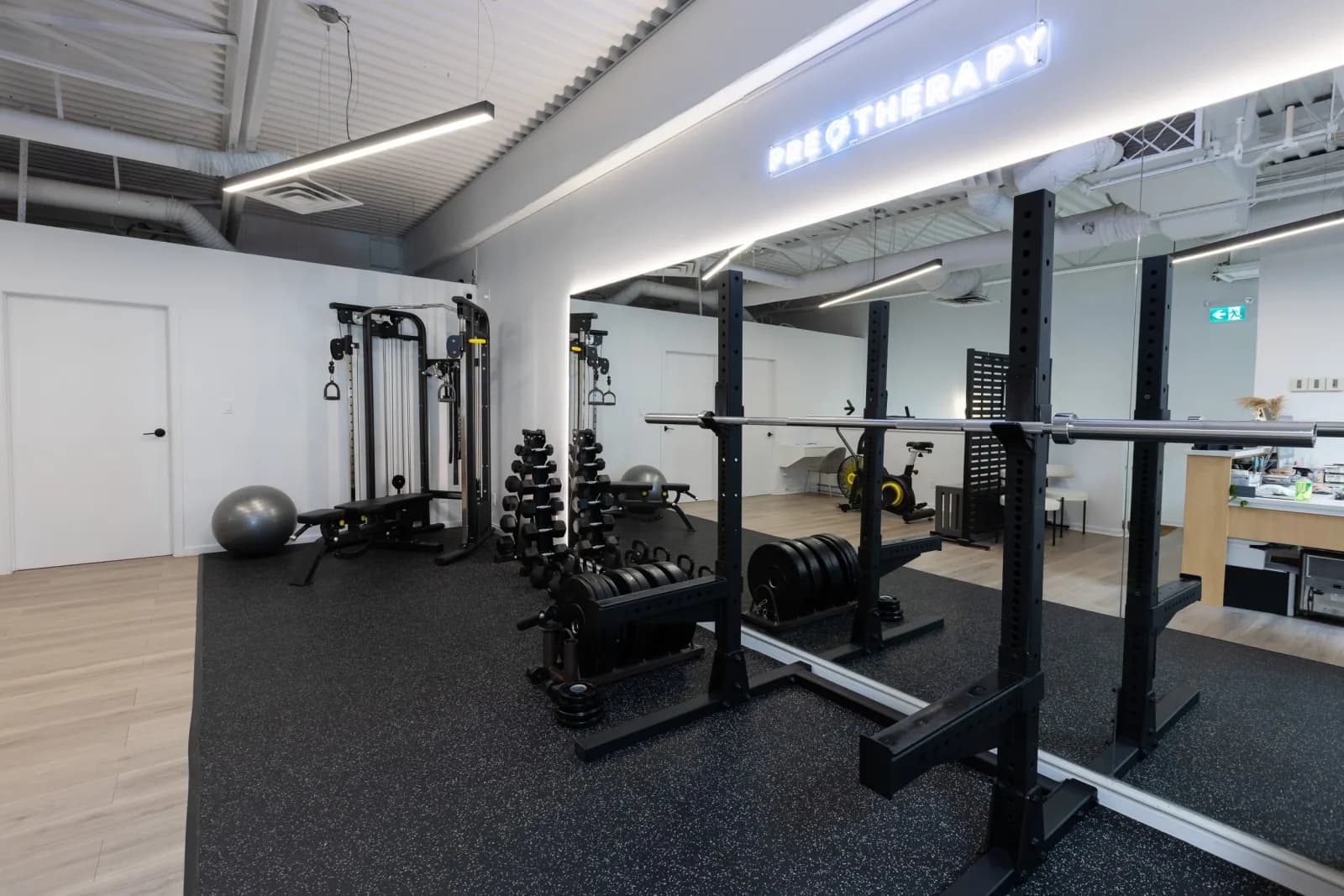Strength and conditioning area of PRE Therapy's rehab gym with racks and free weights