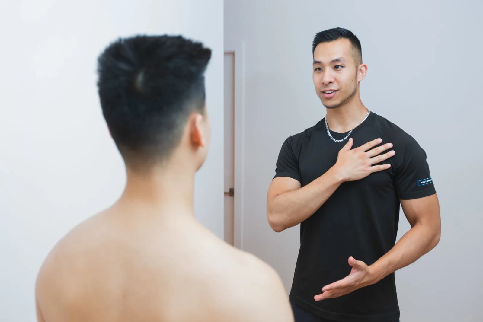 PRE Therapy practitioner explaining posture and movement to a bodybuilding athlete during an assessment.