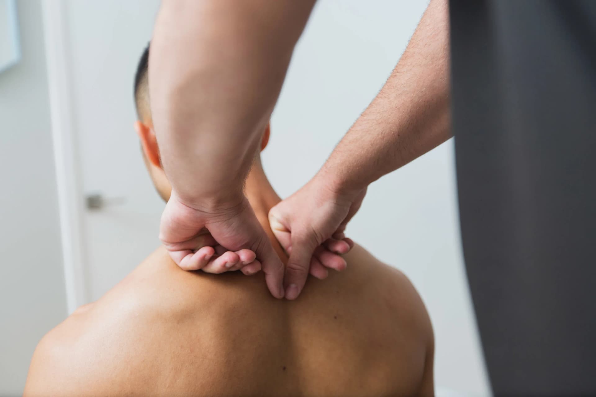A therapist presses both knuckles into the base of a patient's neck and upper back.